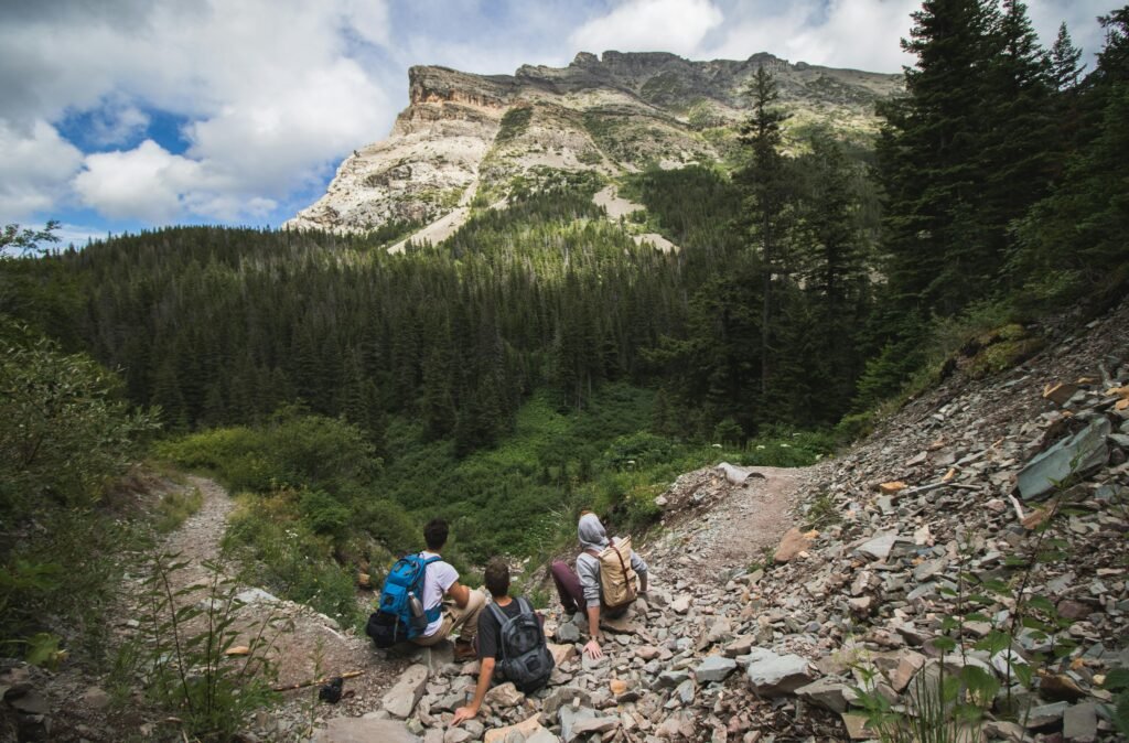 Three hikers sitting along a scenic trail in Montana with lush forests and rocky cliffs in view.